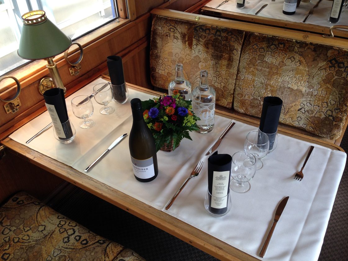 Gedeckter Tisch mit Messinglampe, Wein und Blumen im Speisewagen Gourmino